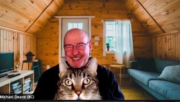 Michael Deane, smiling, with a tabby cat perched against his shoulder.