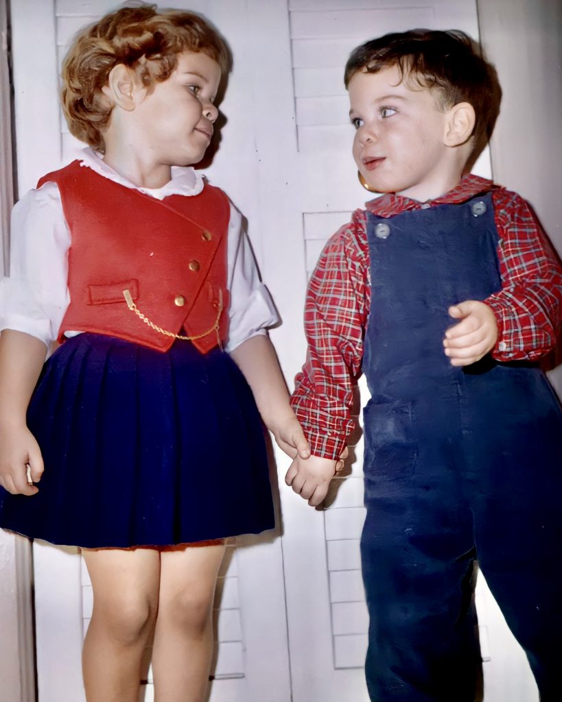 An old photograph of two young children, a girl and a boy, standing hand in hand.